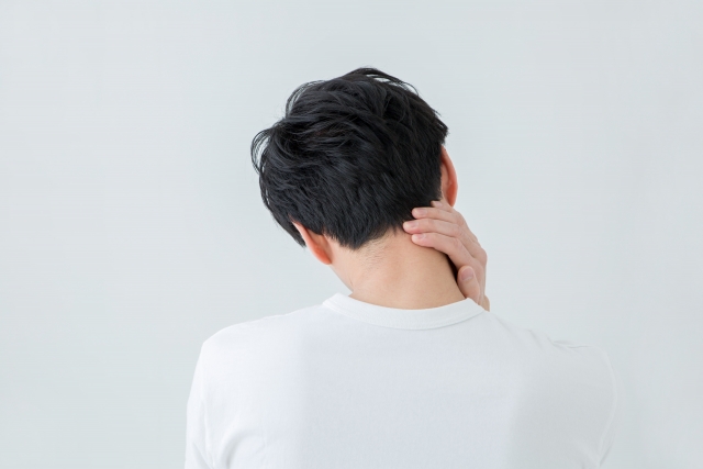 首や肩の疲れを感じて後ろから首筋を押さえる男性の後ろ姿|店長の疲労イメージ