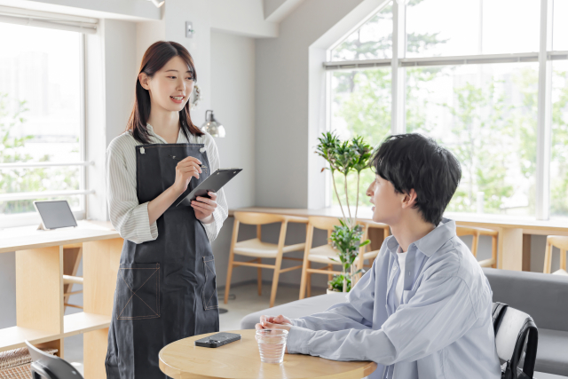 飲食店でスタッフが笑顔で注文を取る様子｜接客の基本動作イメージ