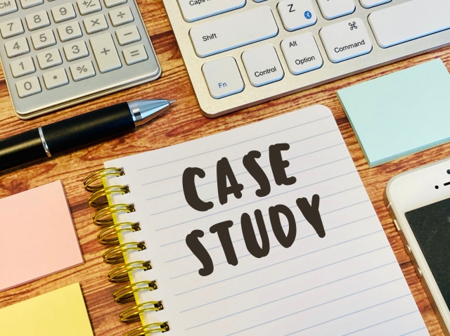 ノートに「CASE STUDY」と書かれたメモと文房具が並ぶデスク。緊急時対応の事例を整理・共有するイメージ。