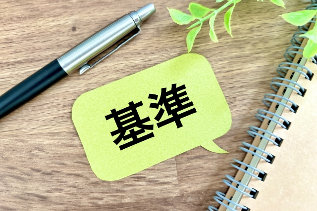 基準と書かれた吹き出しのメモとノート、ペン