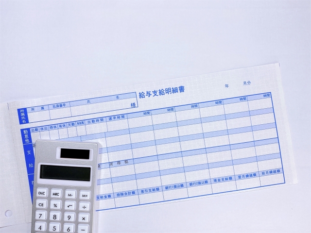 給与明細と電卓の写真。人件費管理とコスト適正化をイメージした画像。