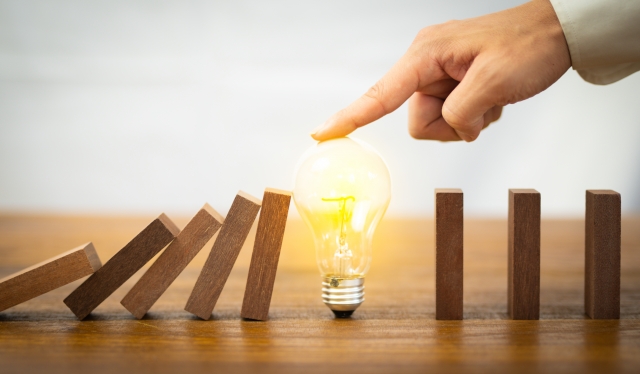 電球でドミノ倒しを止める手の写真。人件費管理の見直しや改善をイメージした画像。