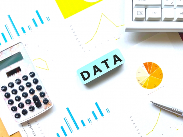 データ資料と電卓を並べて分析している様子を表した画像