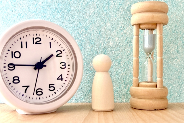 時計と砂時計、木製の人形が並ぶ写真。時間と判断のバランスを象徴している。