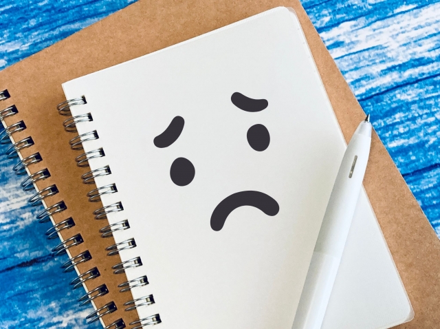 困った表情のイラストが描かれたノートとペンの写真