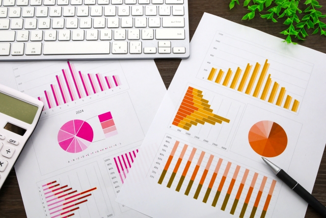 カラフルなグラフや円グラフが印刷された資料と電卓、店長が数字を分析する様子
