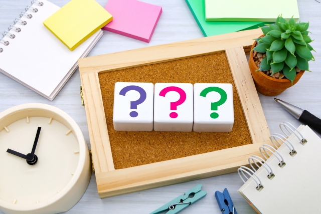 デスクの上に並んだ3つのクエスチョンマークのブロックと時計や観葉植物の写真