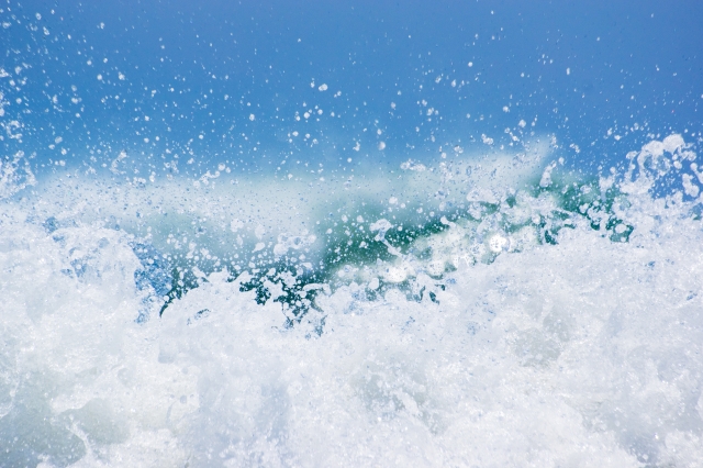 波が大きく崩れた瞬間の写真。強い水しぶきが広がる海の風景。
